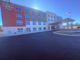 Edifício do Holiday Inn Express & Suites com design moderno, entrada coberta e mastro com a bandeira americana.