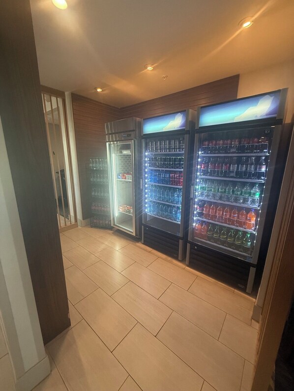 A corridor with three beverage vending machines lined up against a wall, with a tiled floor and a door on the left. - Holiday Inn Express Vidalia by IHG (Vidalia)