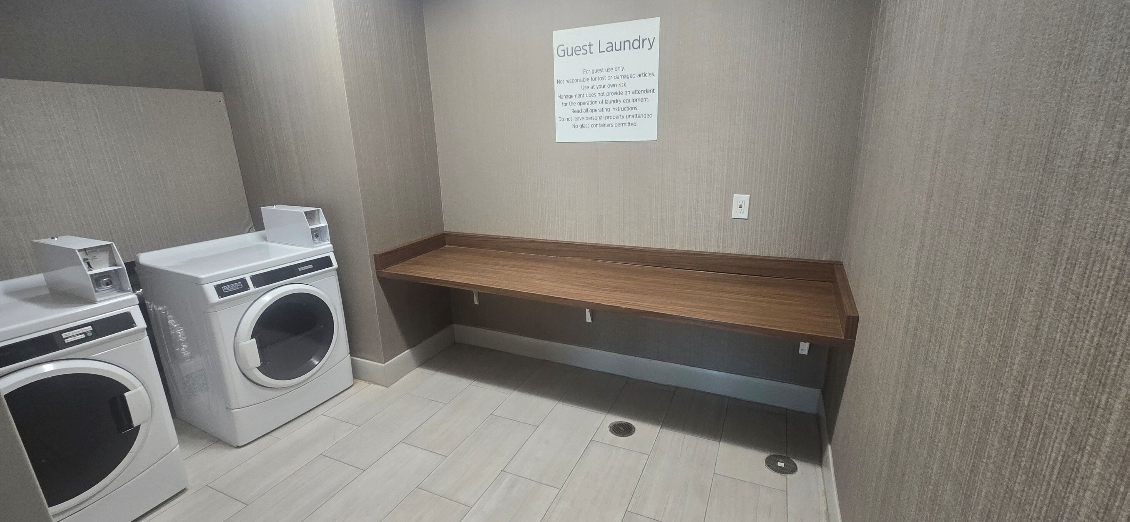 A guest laundry area with a washing machine, dryer, and a wooden bench.