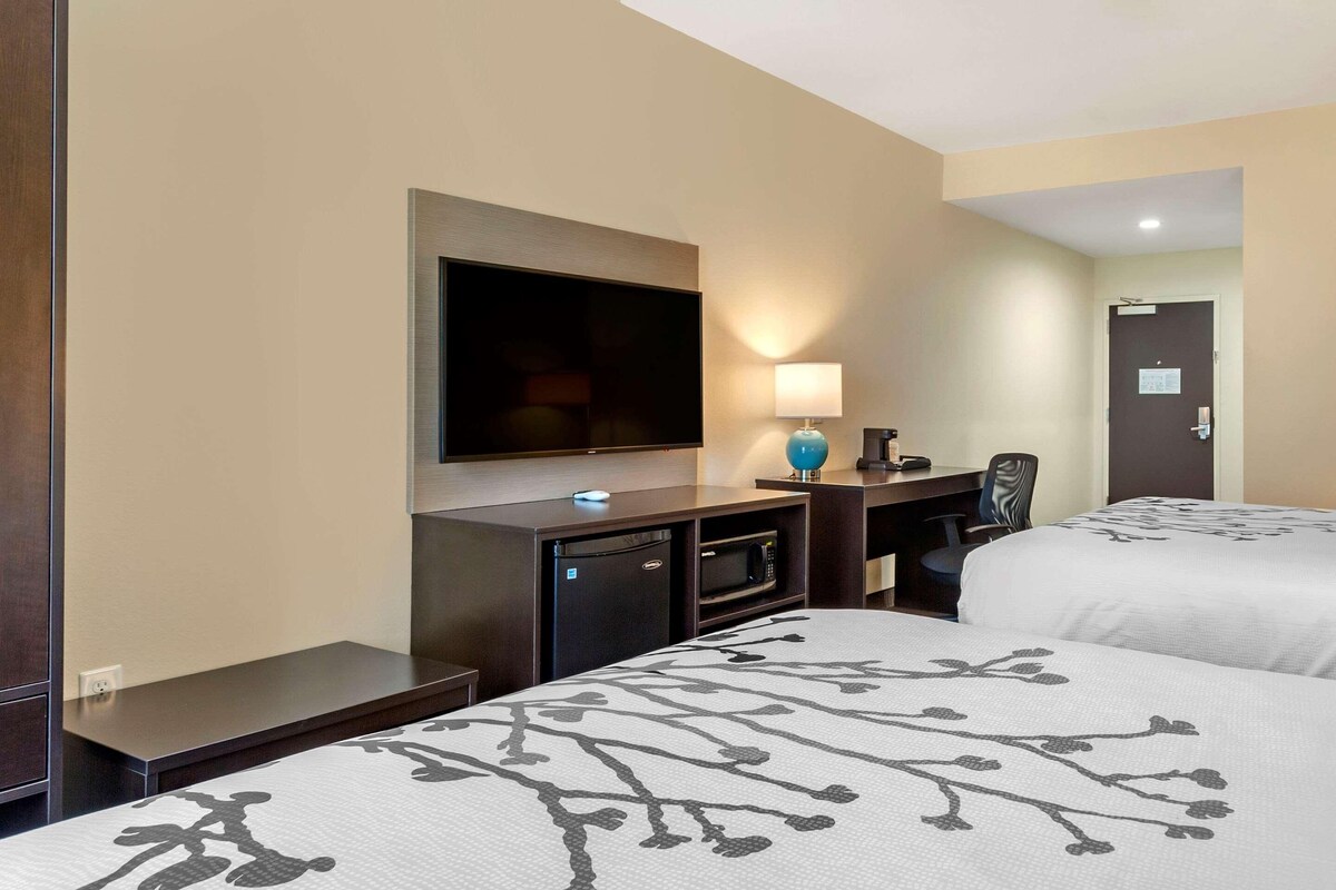 A hotel room with two beds, a TV, a desk with a lamp, and a microwave.