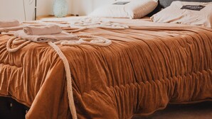 Una cama bien hecha con una cubierta marrón, una lámpara de noche y una alfombra estampada en el suelo.
