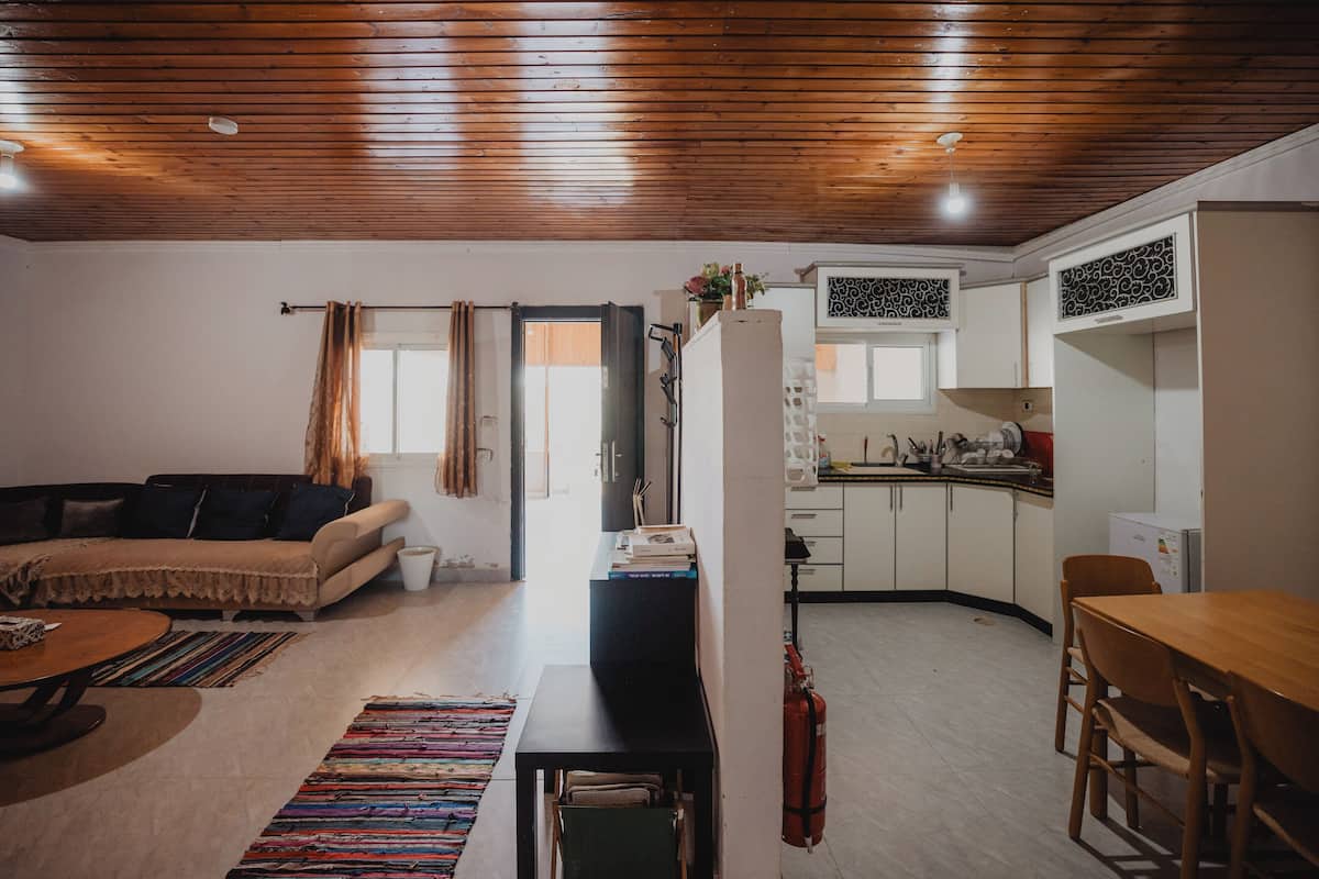 A compact living space with a sofa, a dining table, a kitchen area, and a wooden ceiling.