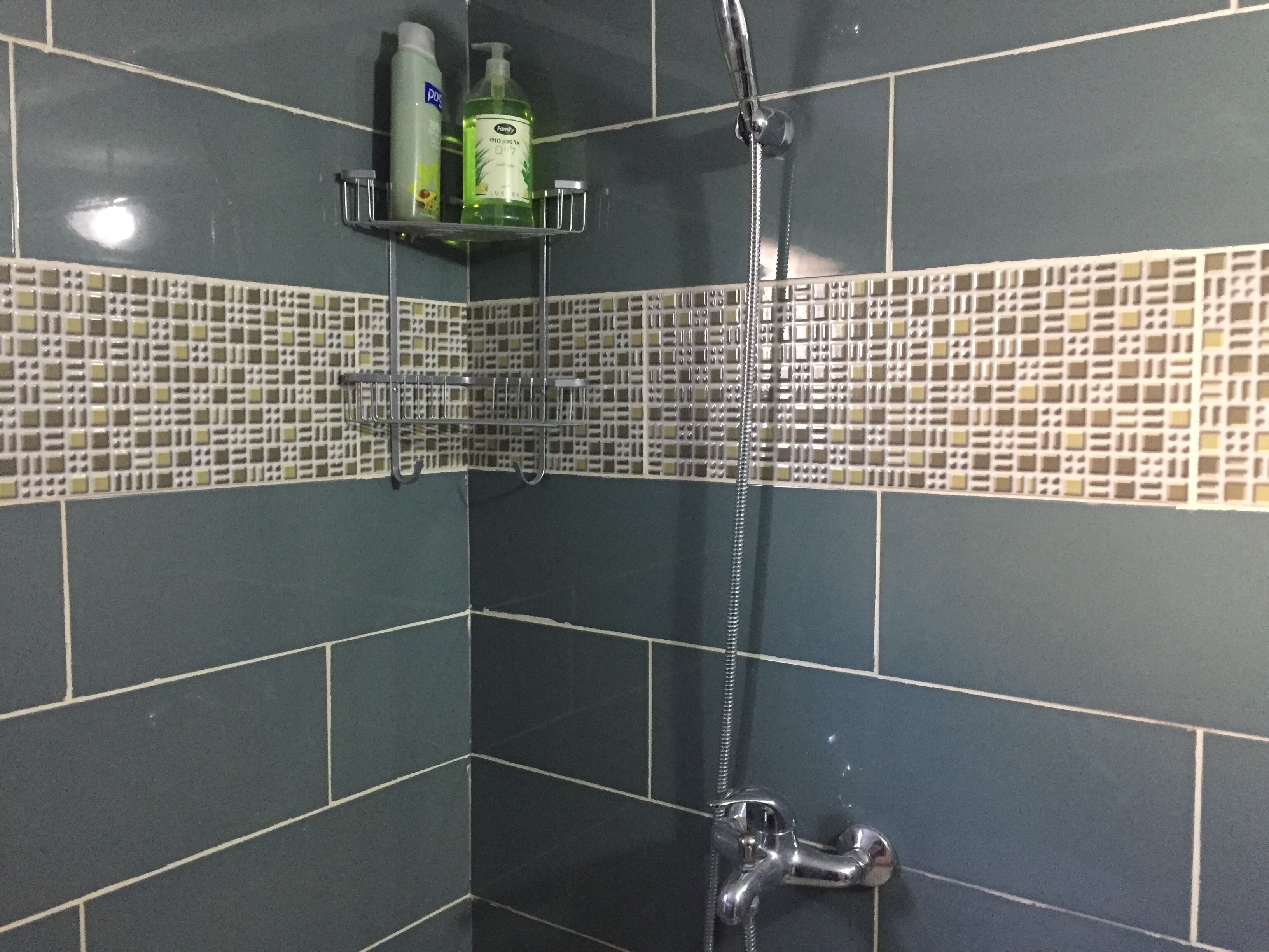 A bathroom with dark tiles, a shower, and a shelf with toiletries.