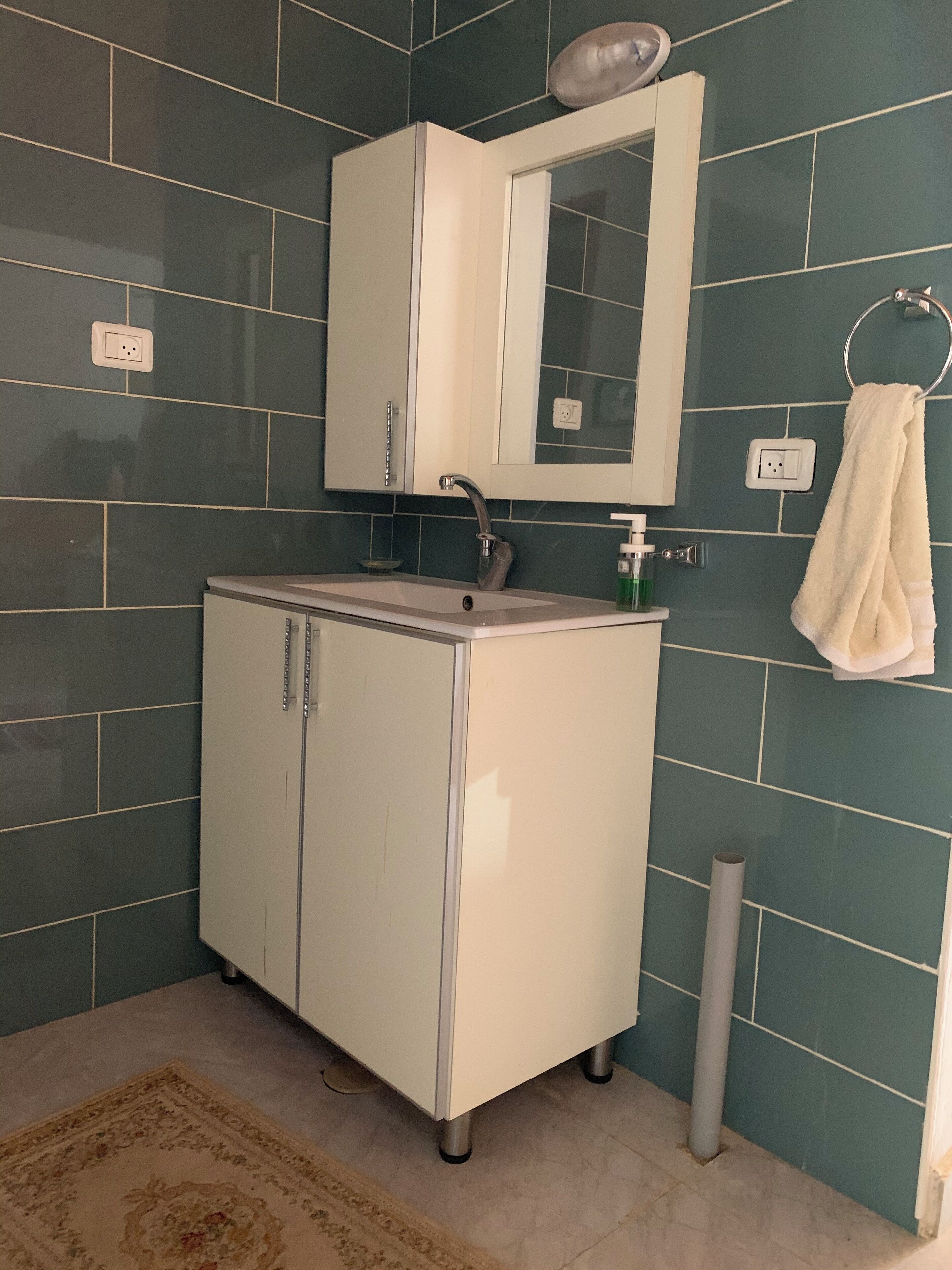 A bathroom with a white cabinet, a mirror, and a towel hanging on the wall.