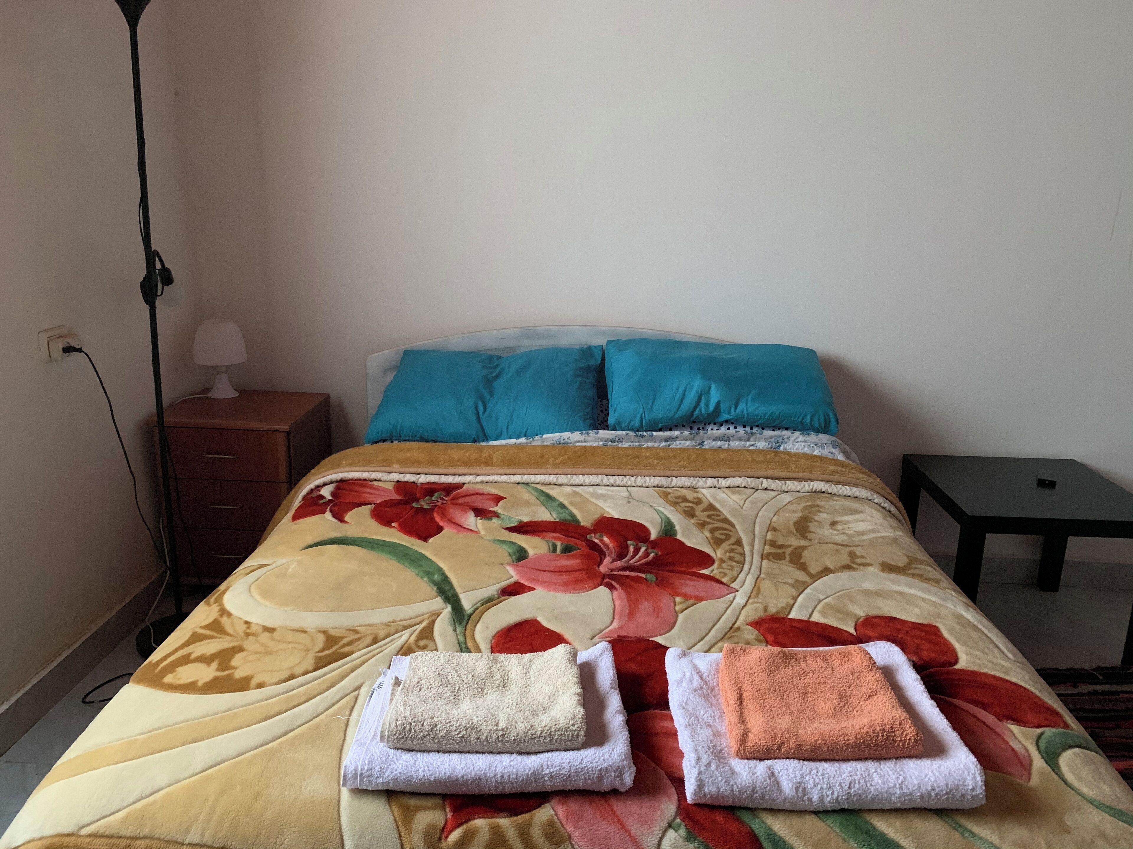 Uma cama com colcha florida, duas almofadas e duas toalhas dobradas.