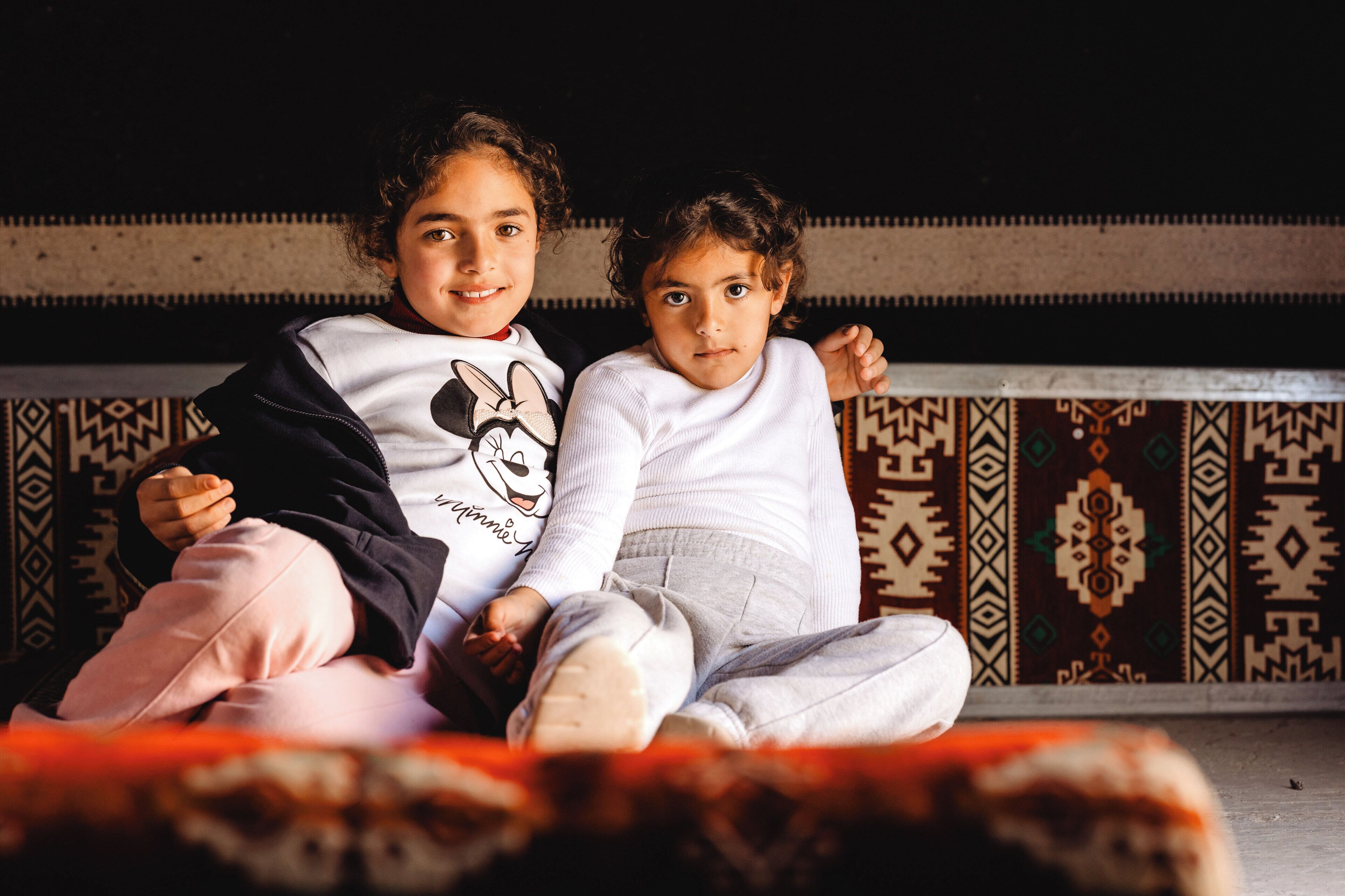Twee kinderen zitten op een vloerkleed met een patroon in een kamer met een klassiek interieur.