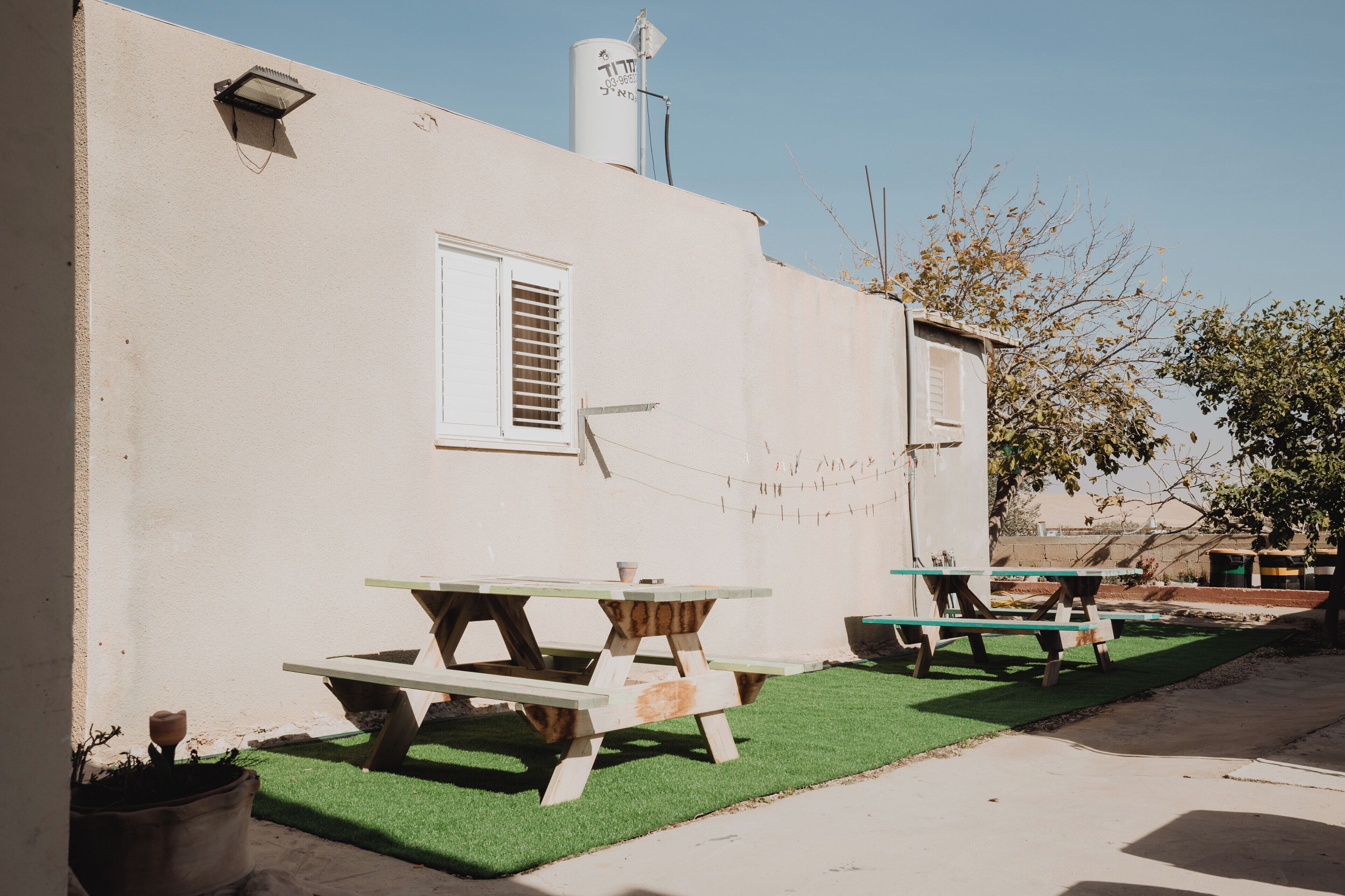 A building with a white exterior, a window with shutters, and two picnic tables on a green lawn.