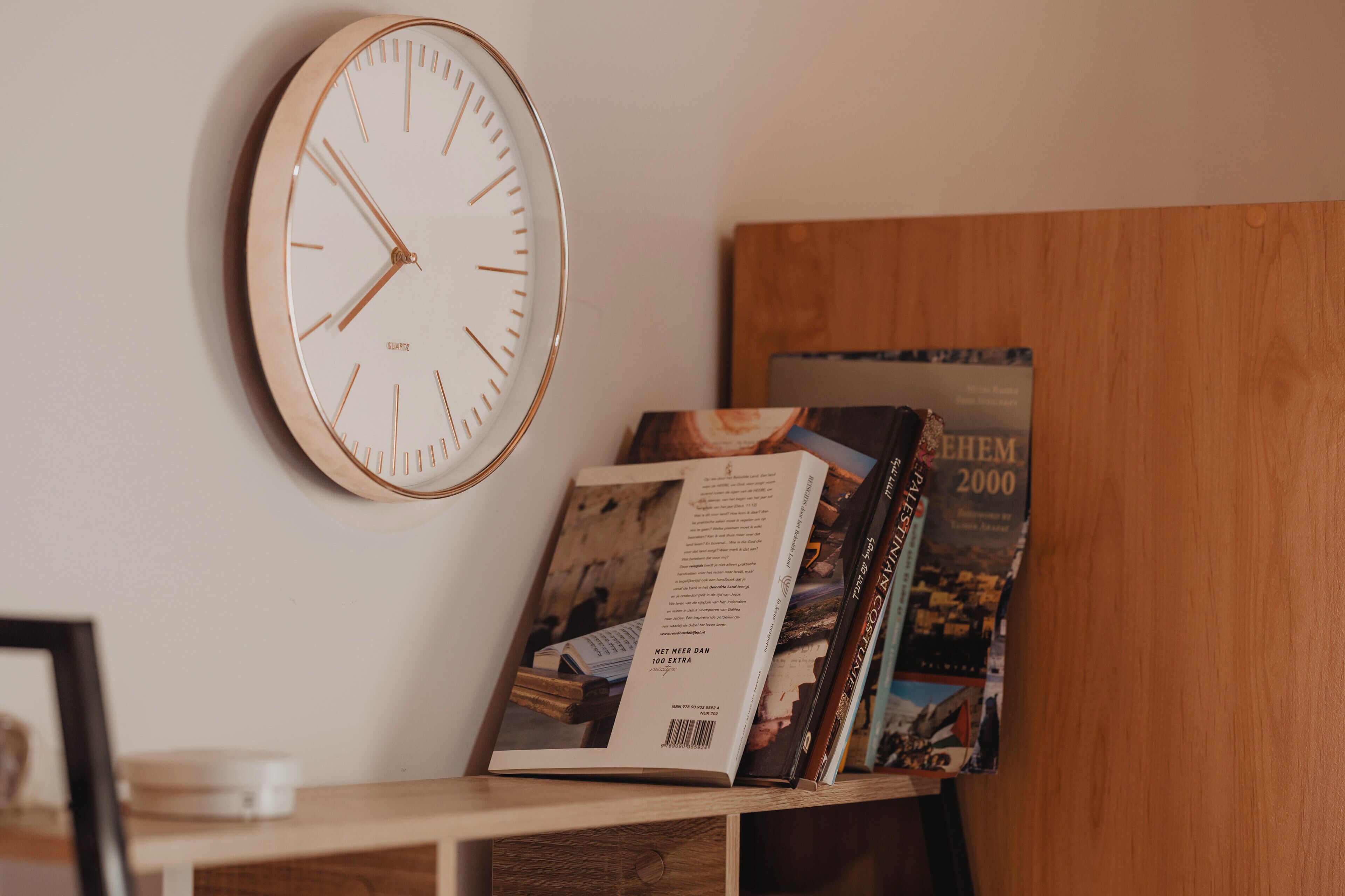Un reloj de pared, un libro y una revista sobre una estantería de madera.