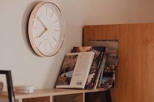 Un reloj de pared, un libro y una revista sobre una estantería de madera.