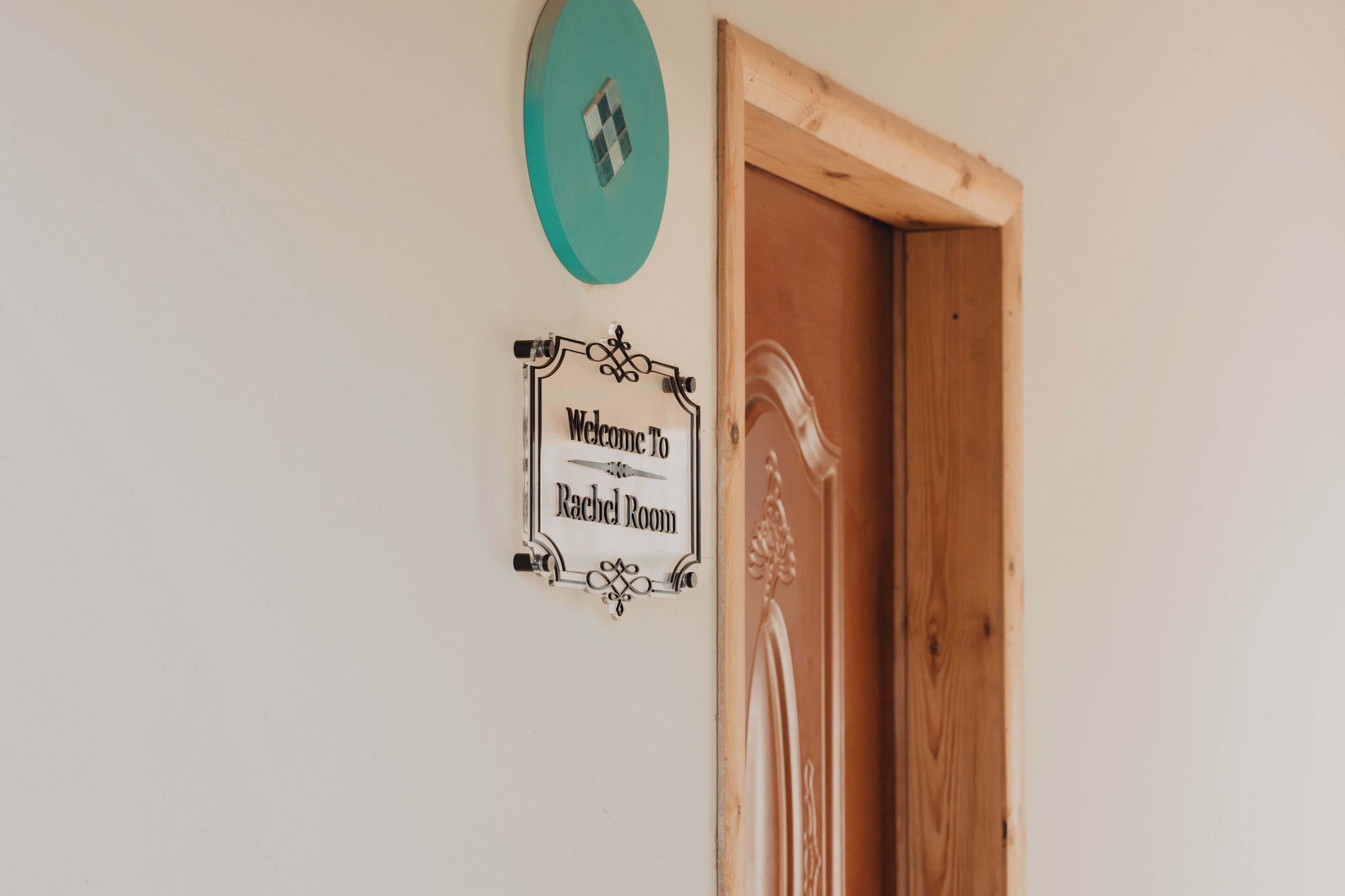 En dörr med en skylt där det står ”Välkommen till Rachel Room” och en turkosfärgad väggdekoration.