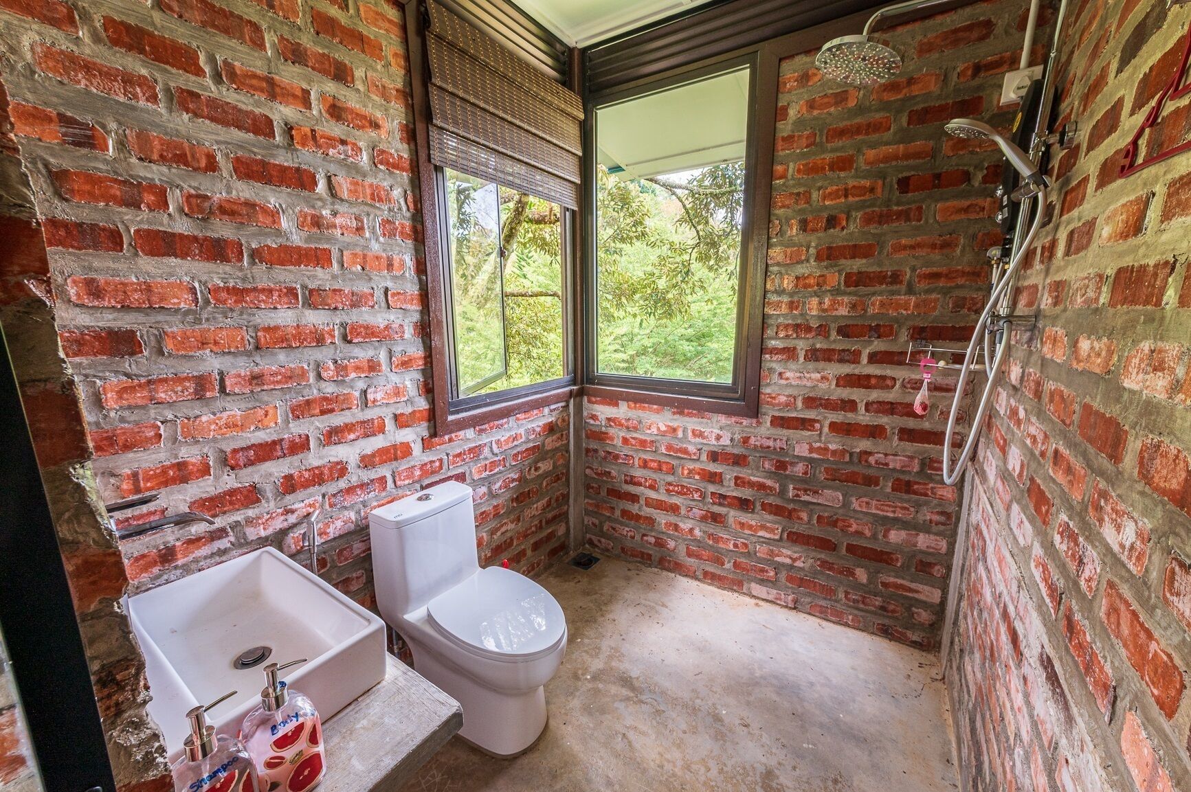 A bathroom with a brick wall, a toilet, a sink, and a shower.