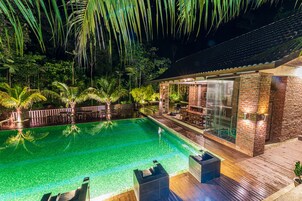 Vista nocturna de una piscina con muelle de madera y zona de patio con paredes de vidrio.