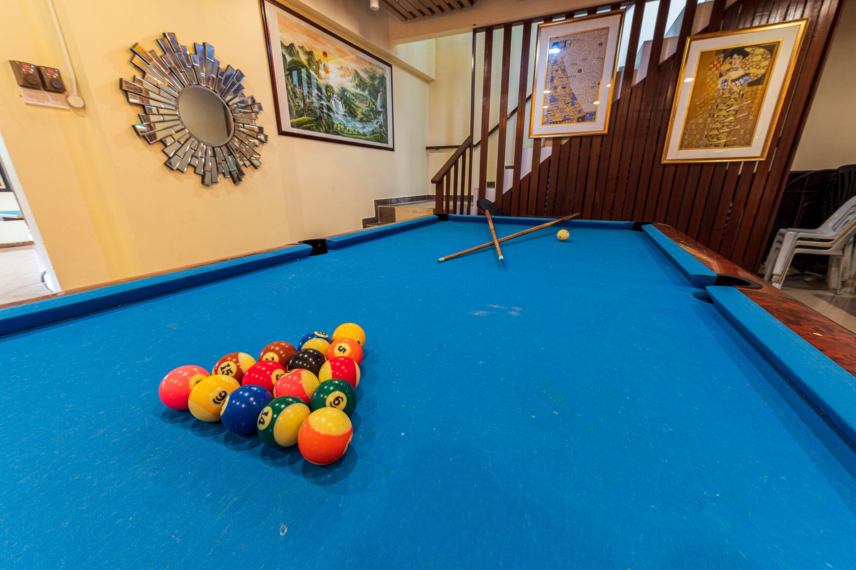A pool table with colorful balls, a mirror, and framed artwork on the walls.