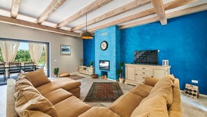 A living room with a blue accent wall, wooden beams, a sofa set, a television, and a fireplace. - Villa Celeste (Umag)