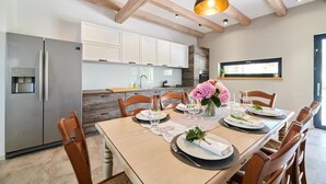 A dining area with a wooden table set for six, a modern kitchen in the background, and a pendant light above. - Villa Celeste (Umag)