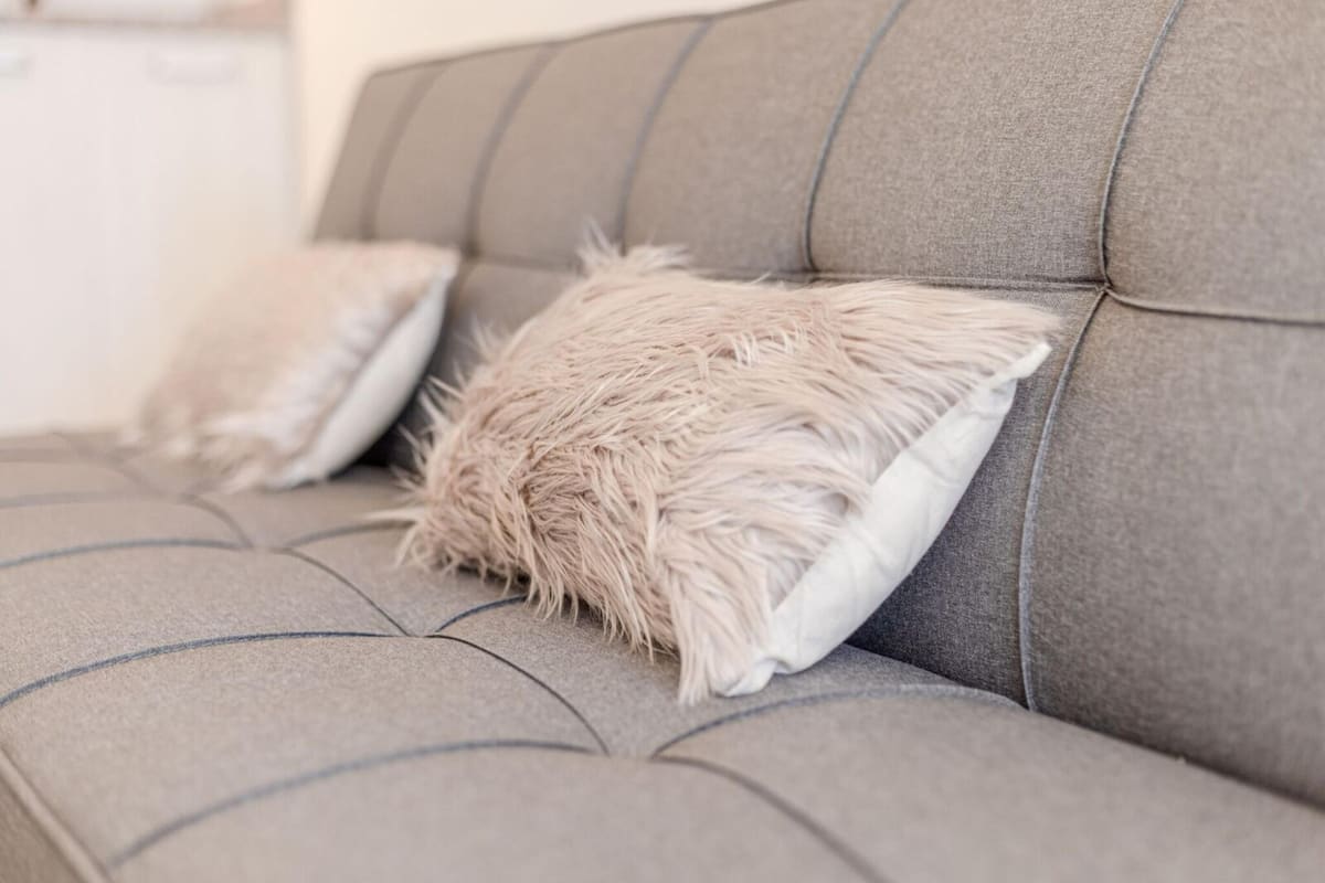 Un sofá gris con un cojín beige texturizado.