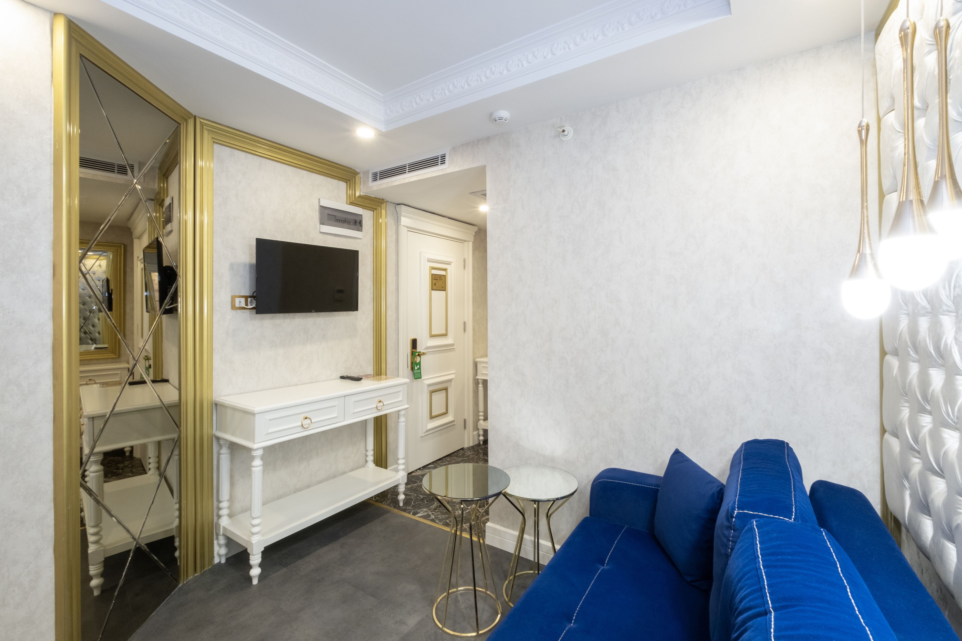 Un salon moderne avec un canapé bleu, une petite table ronde, un téléviseur à écran plat fixé au mur et une console blanche avec des tiroirs.