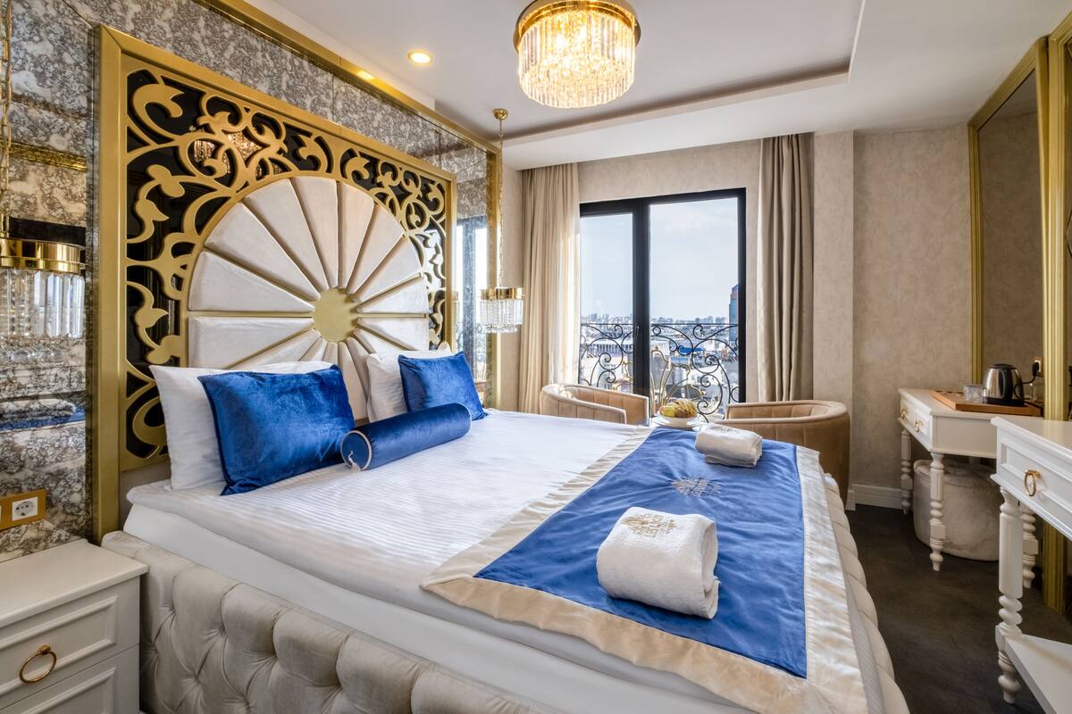 Une chambre d’hôtel luxueuse dotée d’un grand lit, d’une tête de lit décorative, d’un lustre, d’une vue sur la ville et d’un petit coin salon.