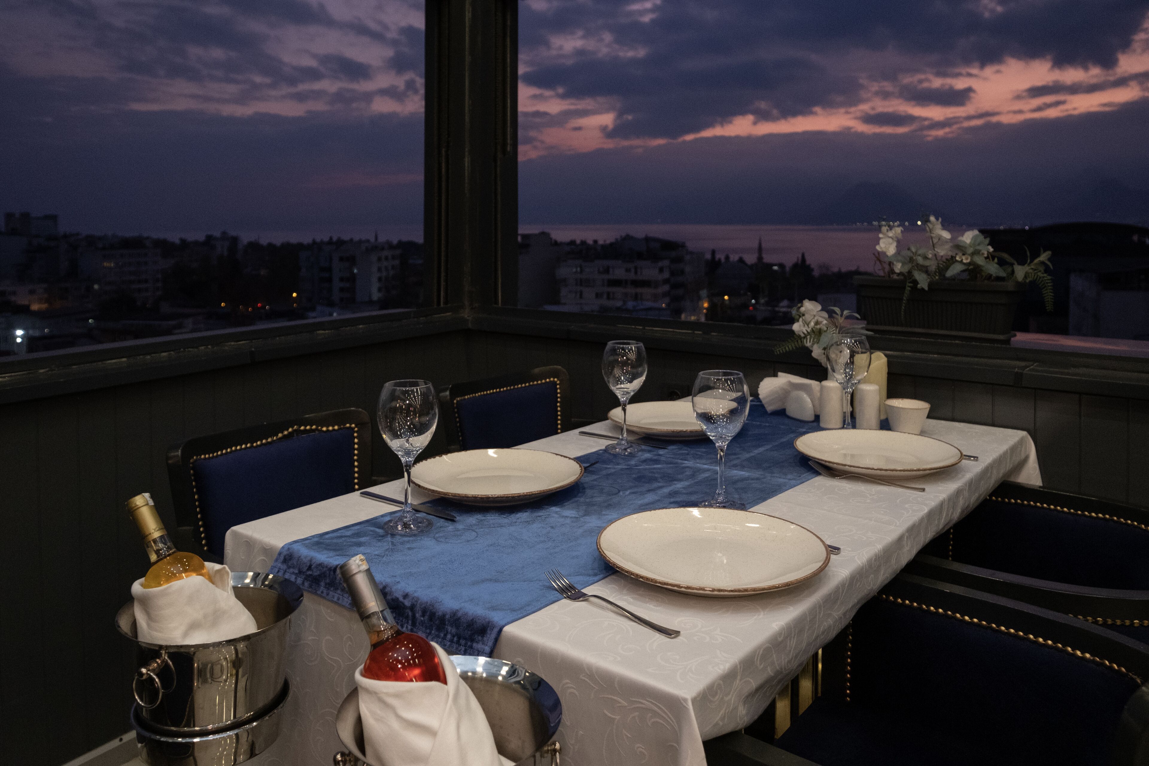 A dining table set for two with a view of the cityscape at dusk.