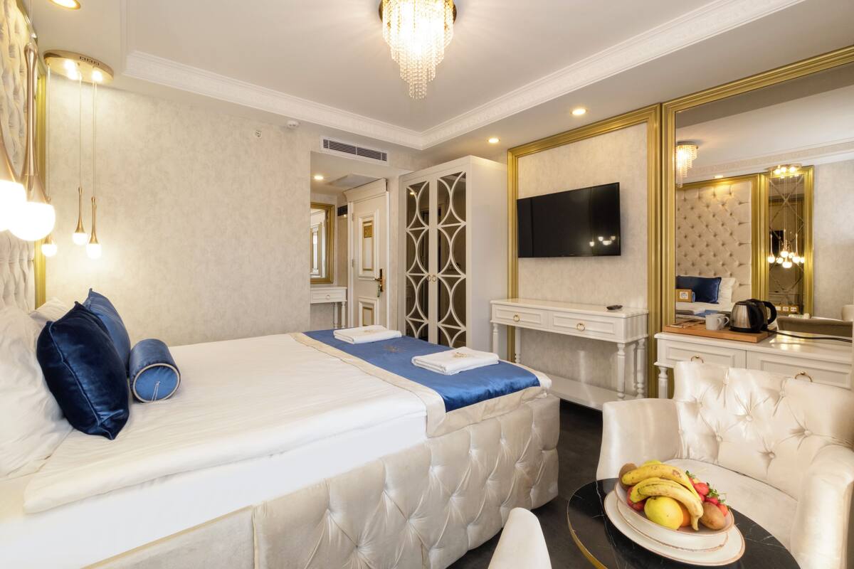 Une chambre à coucher luxueuse, dotée d’un grand lit, d’une télévision, d’un miroir et d’une table à manger agrémentée de fruits.