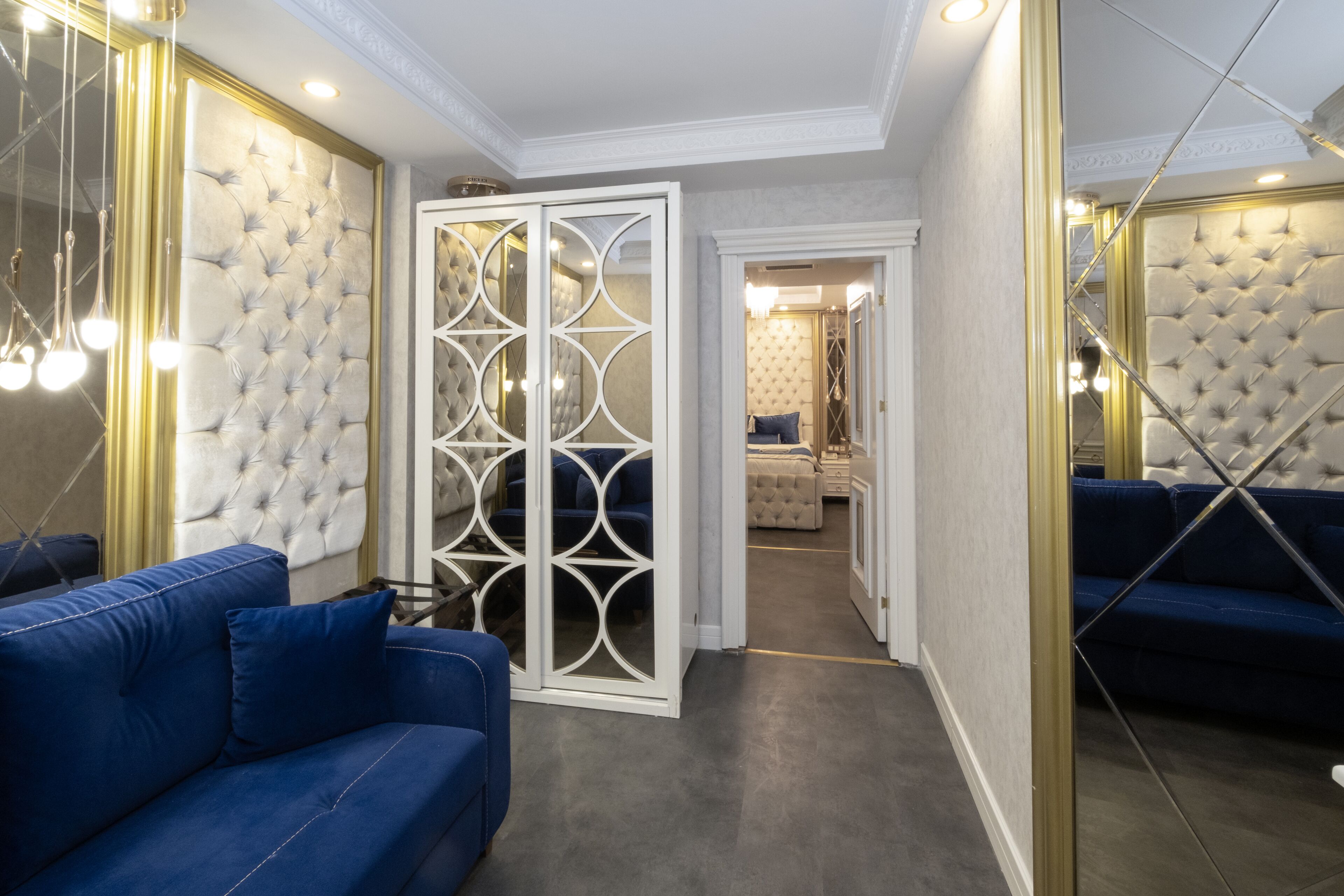 Una habitación con sofá azul, armario con espejo y cabecera acolchada.