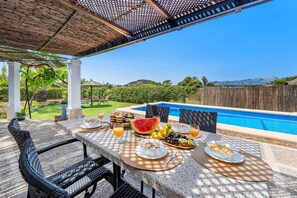Disposição para café da manhã ao ar livre com vista para a piscina, incluindo mesa com itens de café e cadeiras.