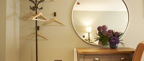 A room with a coat rack, a mirror, a wooden dresser, and a chair.