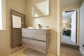 A bathroom with a wooden vanity, a towel rack, and a mirror with lights. - Valentinos Restaurant With Rooms (Ripon)
