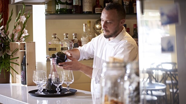 A bar area with a counter, bar tools, and a variety of bottles. - Valentinos Restaurant With Rooms (Ripon)