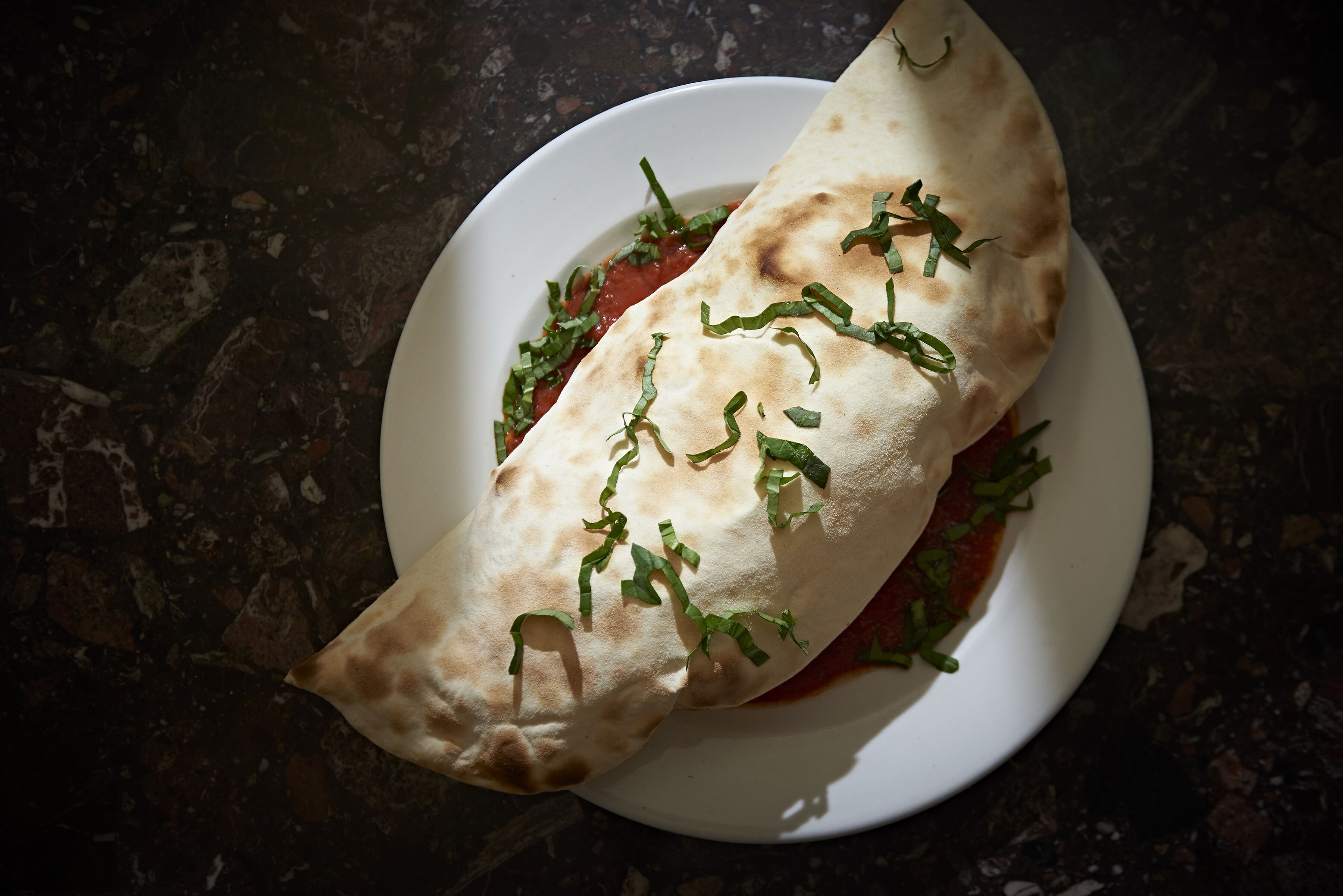 Una masa plana con salsa de tomate y hierbas verdes sobre un plato blanco.
