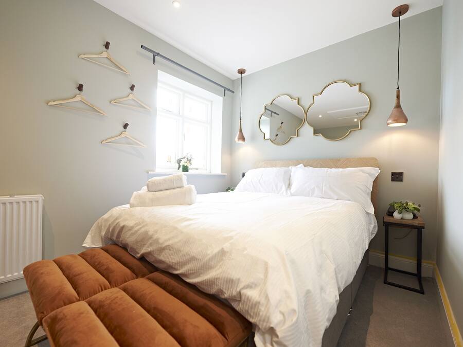 Ein Schlafzimmer mit Bett, einer Bank, einem Heizkörper, einem Fenster und Wandspiegeln.