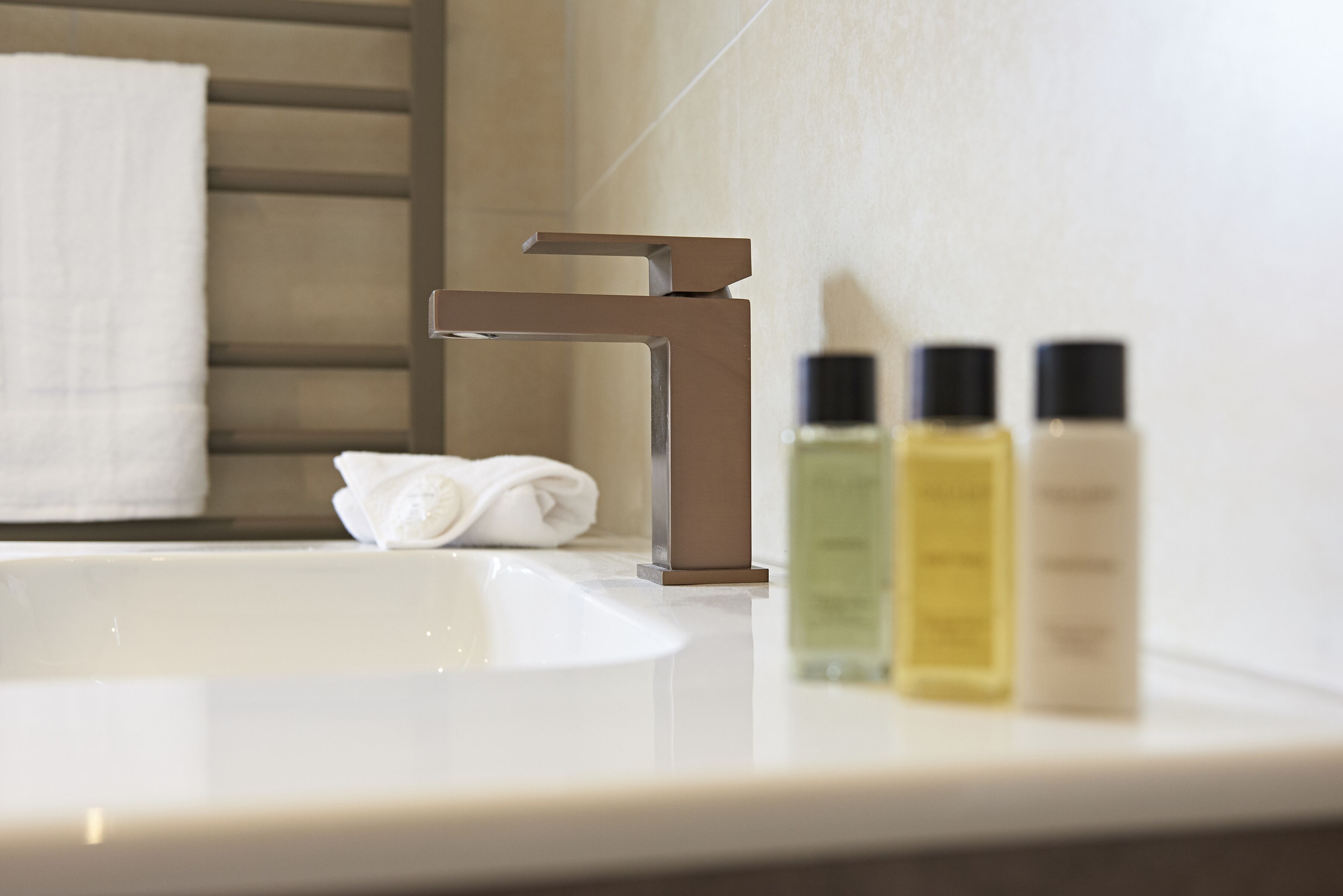 Un lavabo in bagno con un rubinetto moderno, un asciugamano e tre flaconi di articoli da toilette.