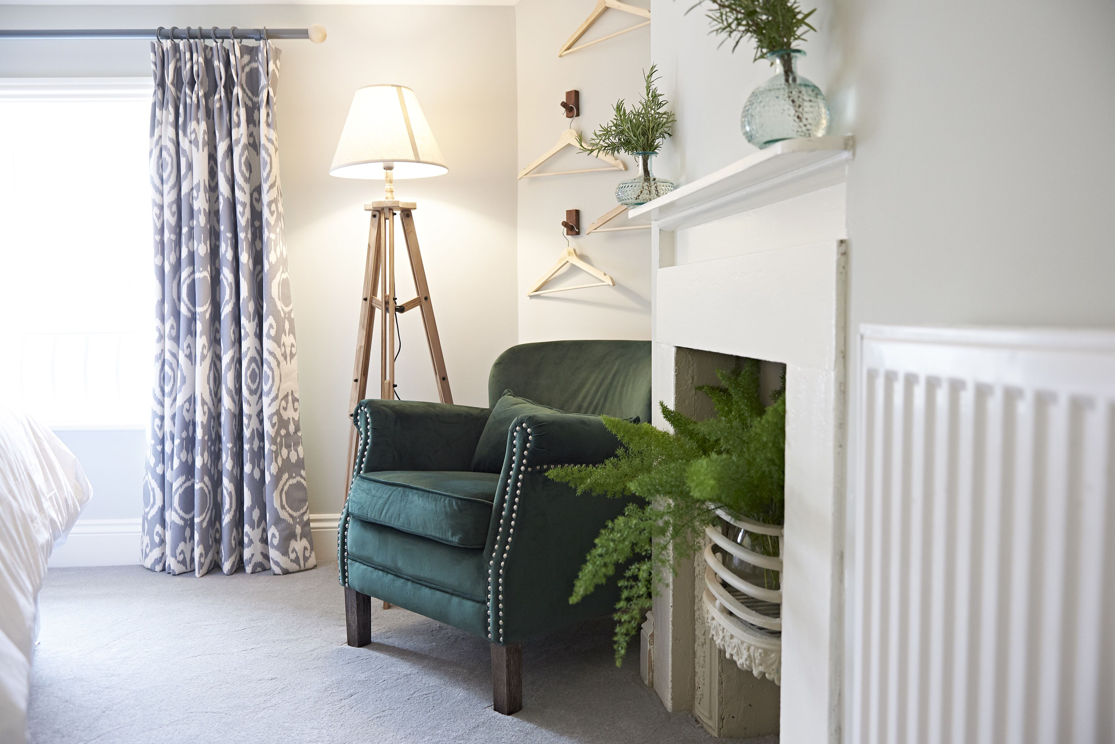 Une pièce avec un fauteuil vert, une lampe sur pied, une cheminée et une plante.