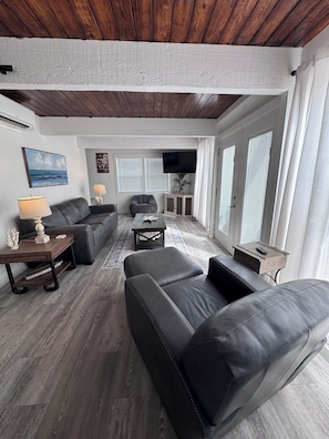 A modern living room with a wooden ceiling, a grey sofa, a coffee table, and a TV mounted on the wall.