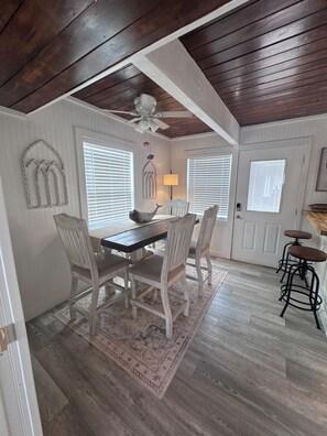 A dining area with a wooden table and chairs, a ceiling fan, and a patterned rug.