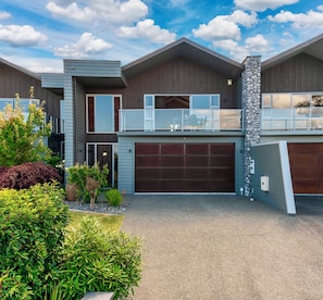 A modern two-story house with a garage, a balcony, and a stone pillar.
