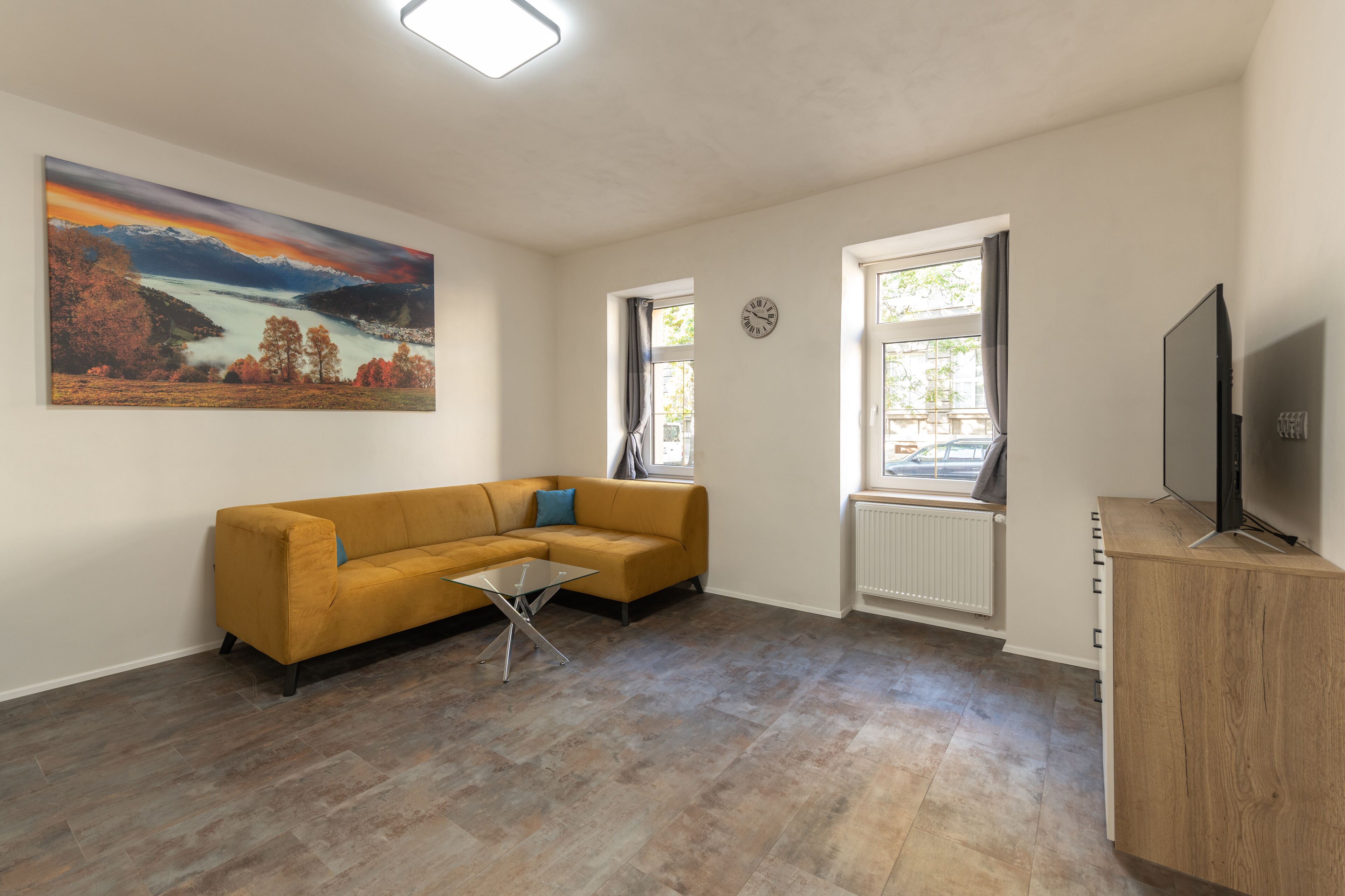 A living room with a sofa, a coffee table, a painting, a TV, and a window.