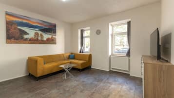A living room with a sofa, a coffee table, a painting, a TV, and a window.