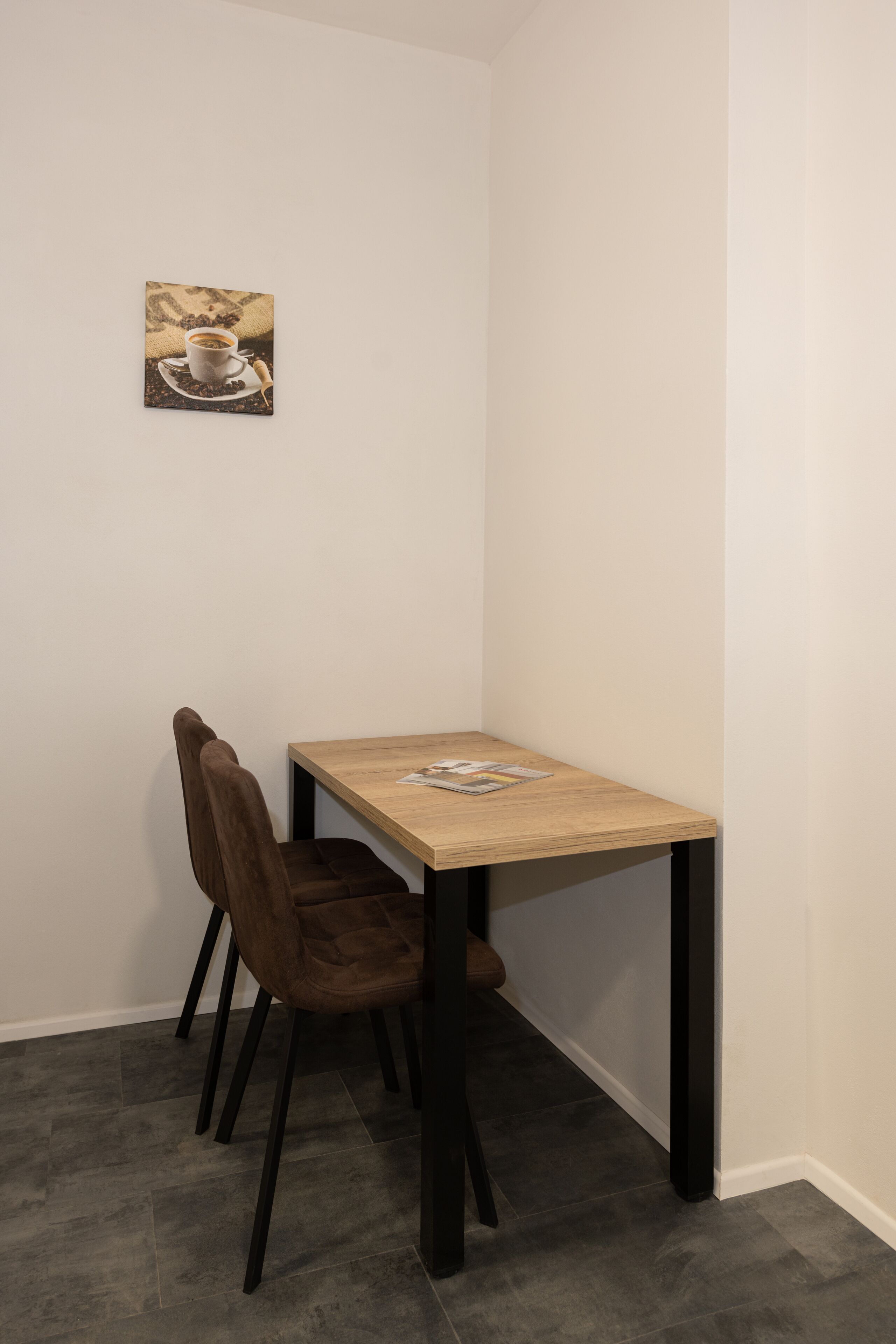 A small dining area with a wooden table, a brown chair, and a single framed picture on the wall.