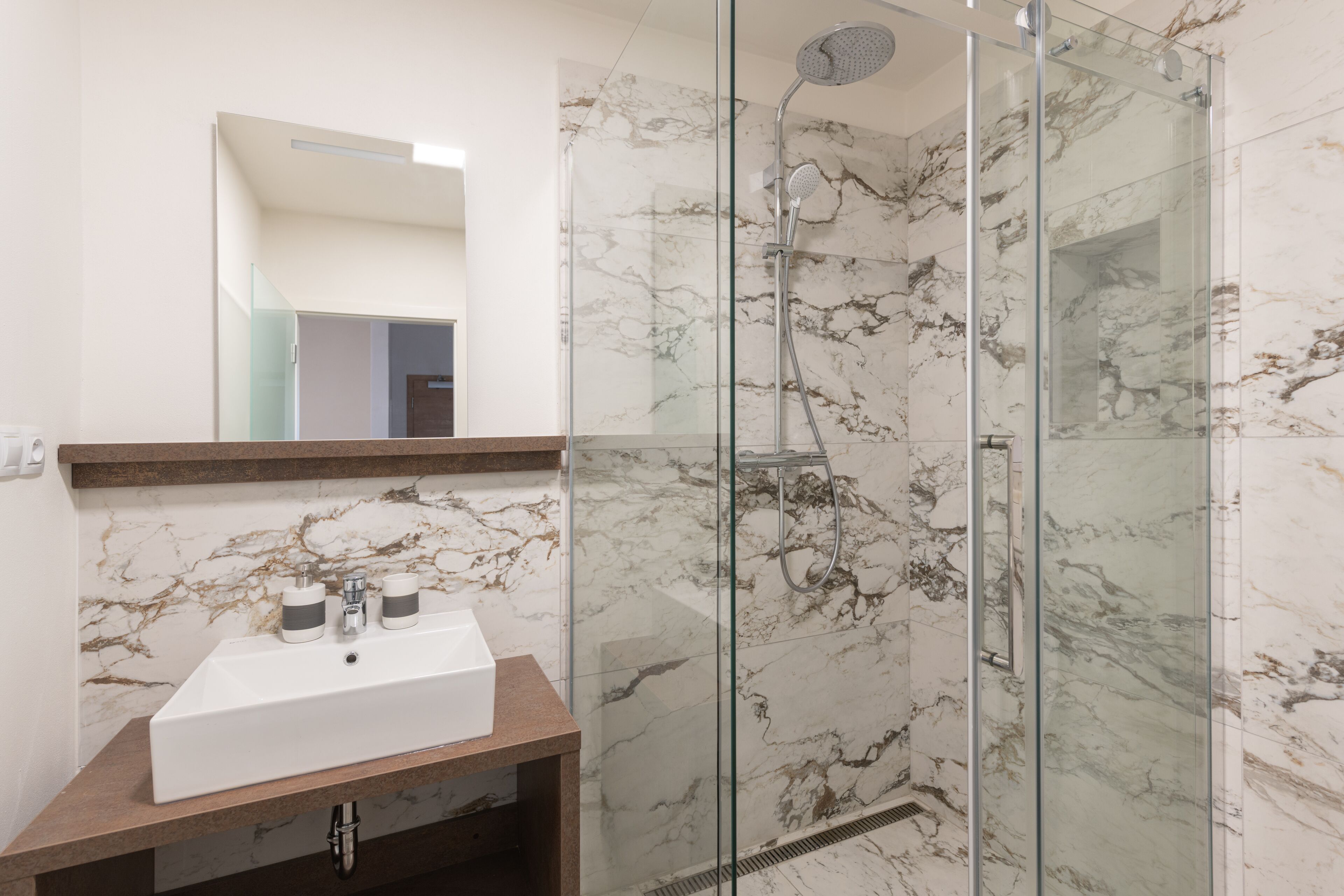 A modern bathroom with a marble backsplash, a white sink, and a glass-enclosed shower.