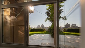 A view through a window of a building with a paved outdoor area, greenery, and distant buildings. - Apartsee Wellness Plzeň (Plzen)