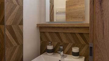 A bathroom with a white sink, two soap dispensers, a mirror, and a wooden wall with a herringbone pattern.