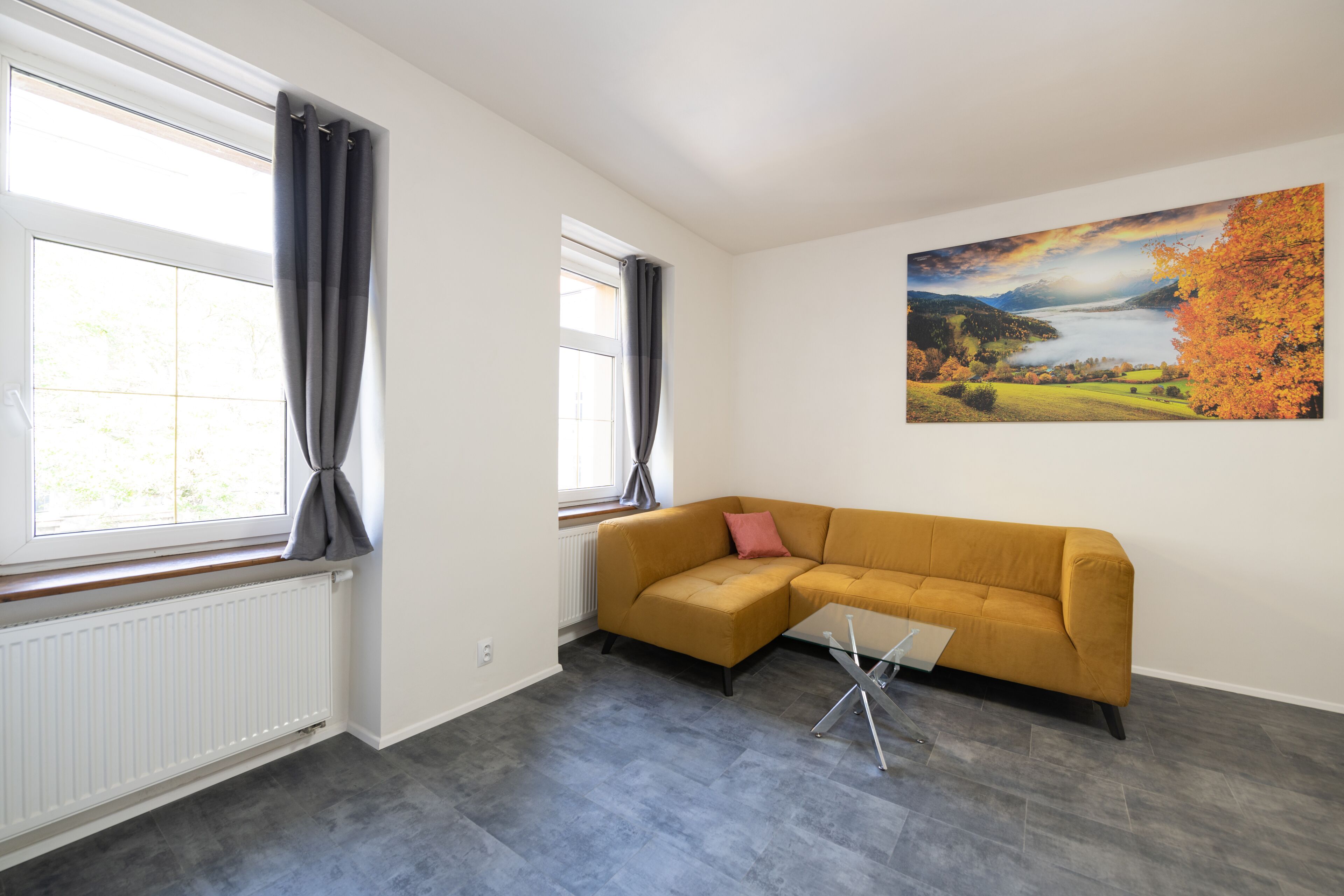 A modern living room with a large window, a sofa, and a painting on the wall.