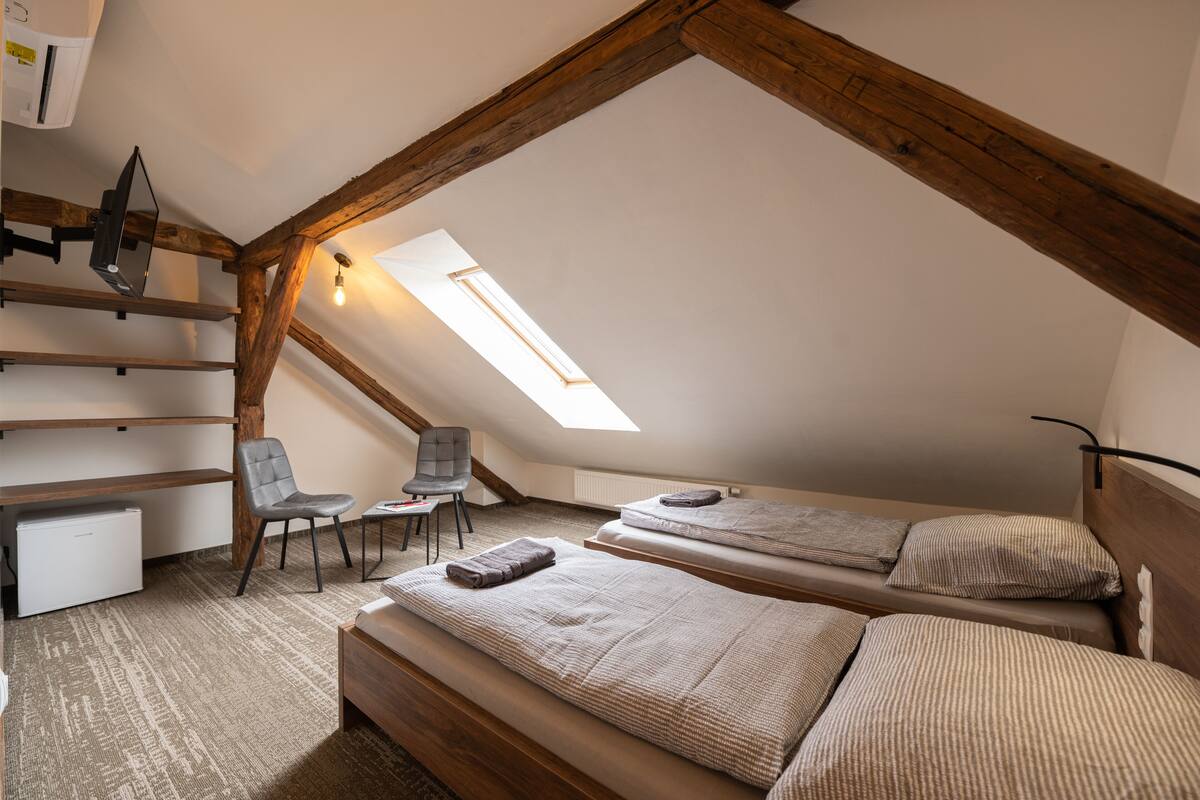 A cozy attic bedroom with two beds, a desk, and a chair.