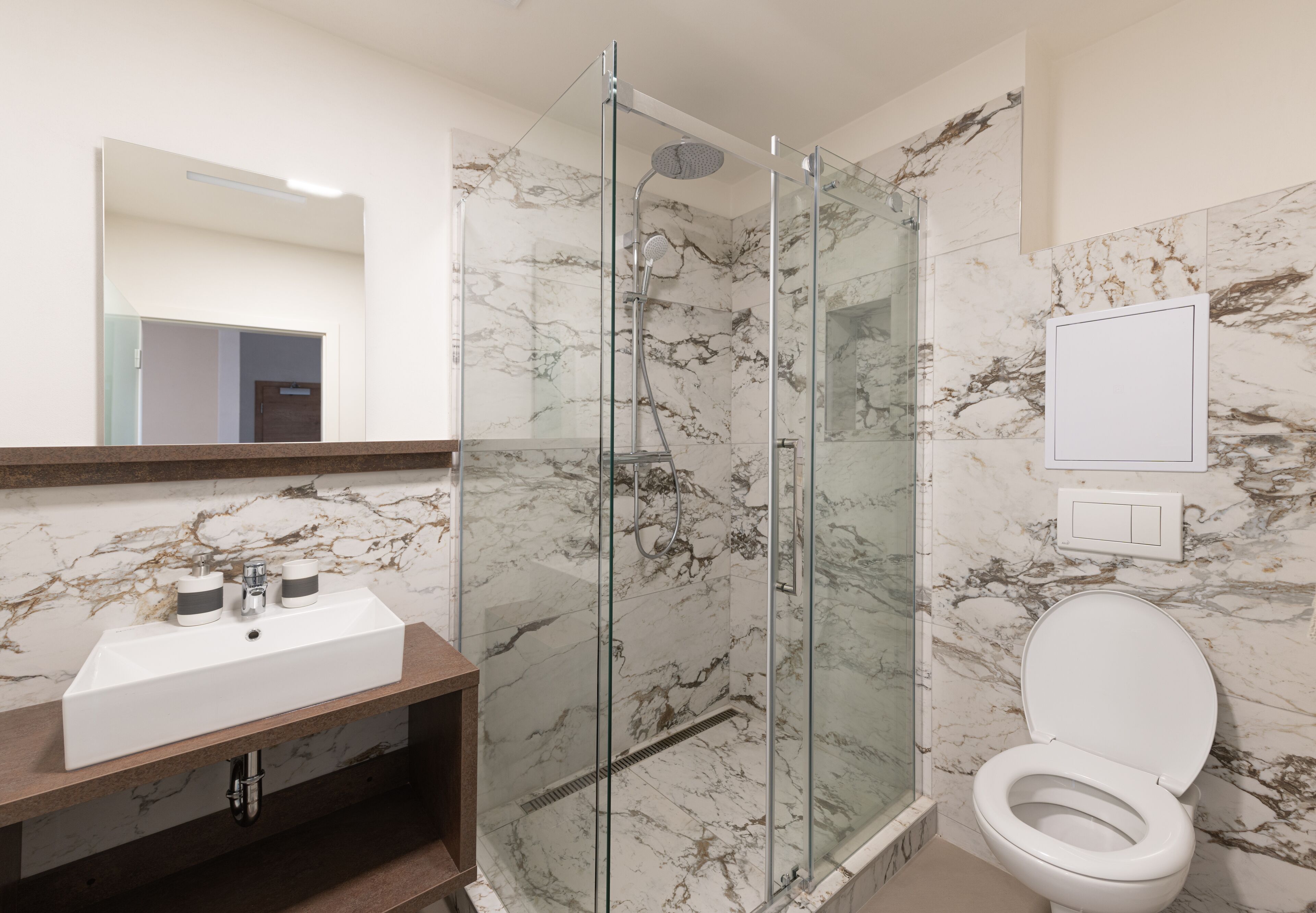 A bathroom with a glass-enclosed shower, a white sink with two faucets, and a toilet.