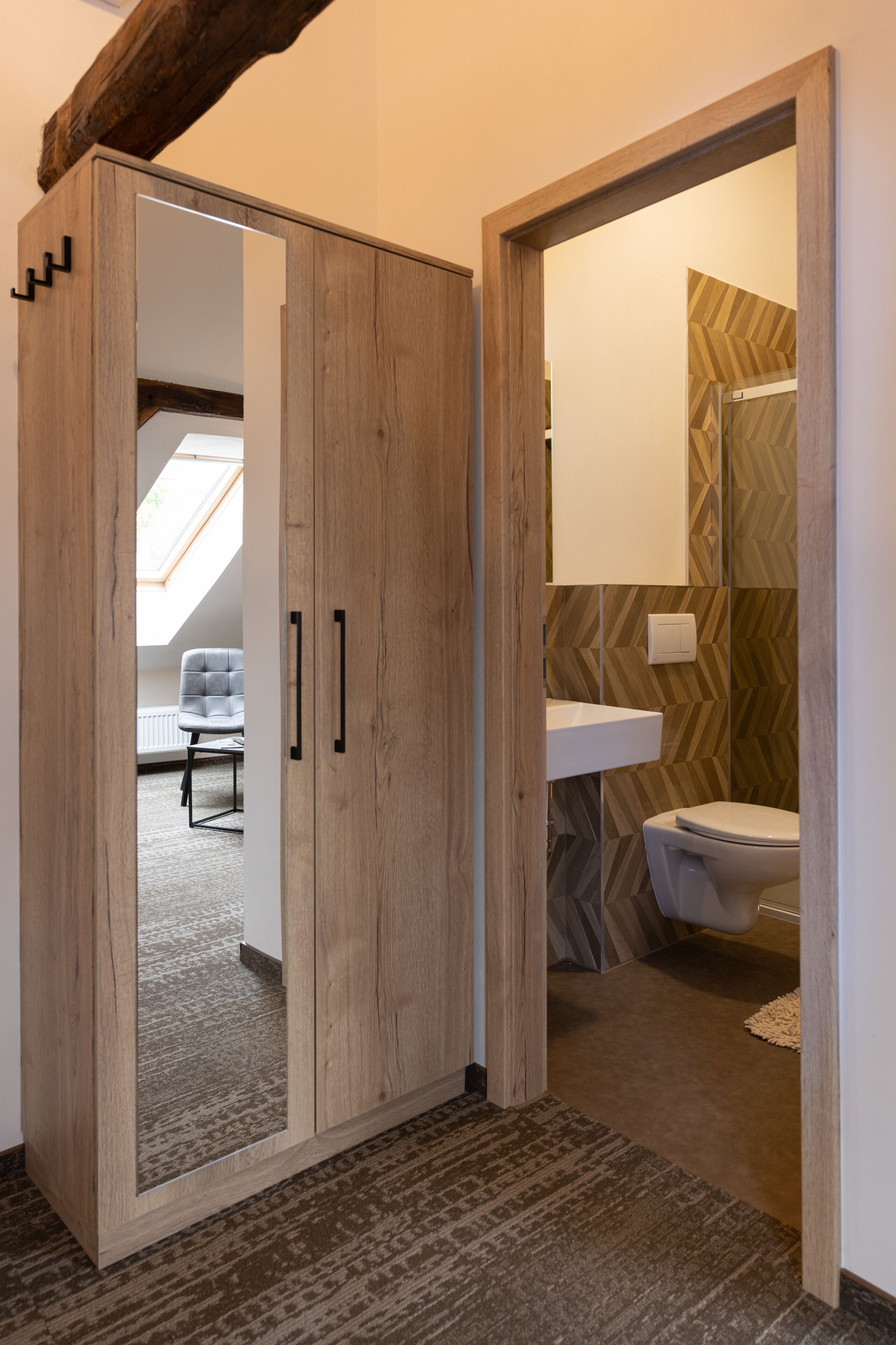 A wooden wardrobe with a mirrored door, a bathroom with a herringbone-patterned wall, and a skylight in the adjacent room.