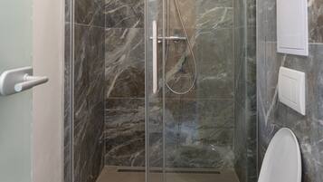 Un bagno moderno con doccia vetrata, un water bianco e pareti in marmo.