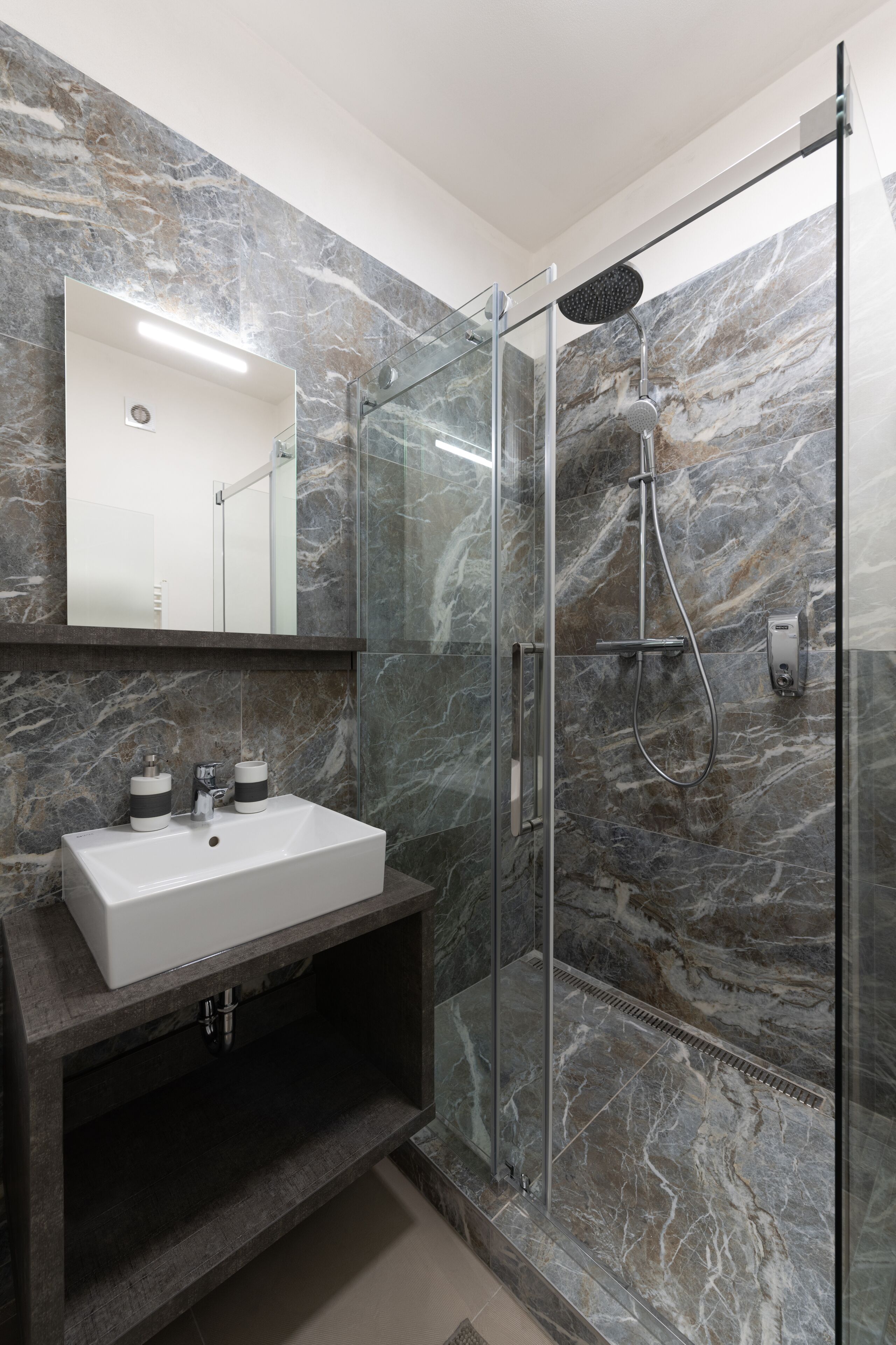 Un baño moderno con ducha envuelta en vidrio, un lavabo blanco y un salpicadero de mármol.