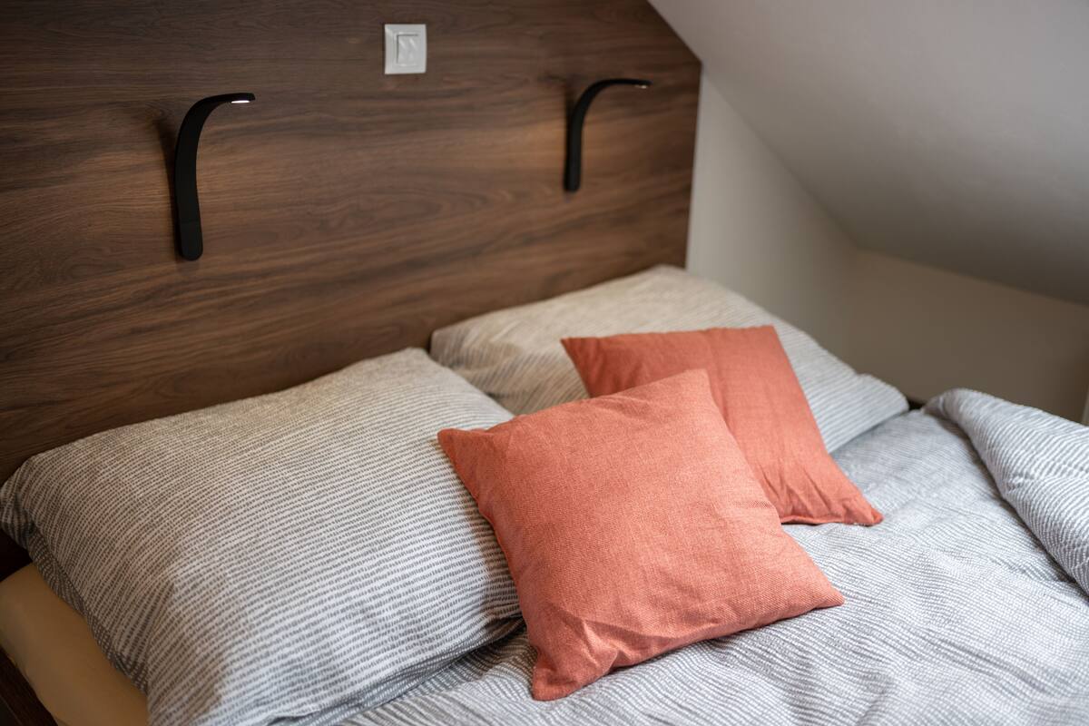 A bed with two pillows, a wooden headboard, and a light switch.