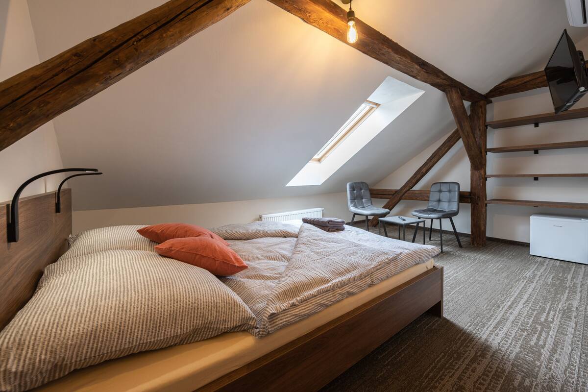 A loft bedroom with a sloped ceiling, a skylight, a bed with pillows, a desk, and a chair.